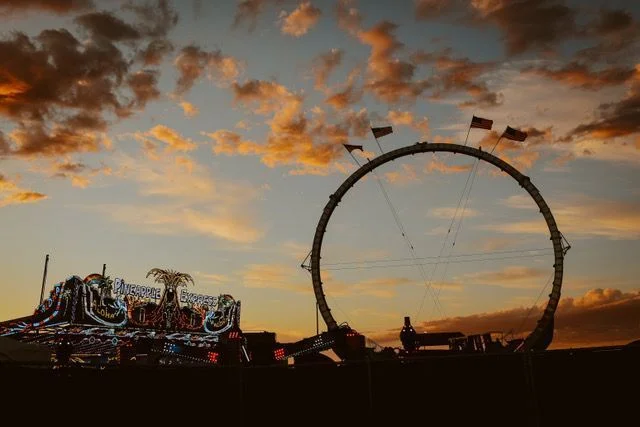 Carnival rides appear in silhouette before an orange sky at sunset.