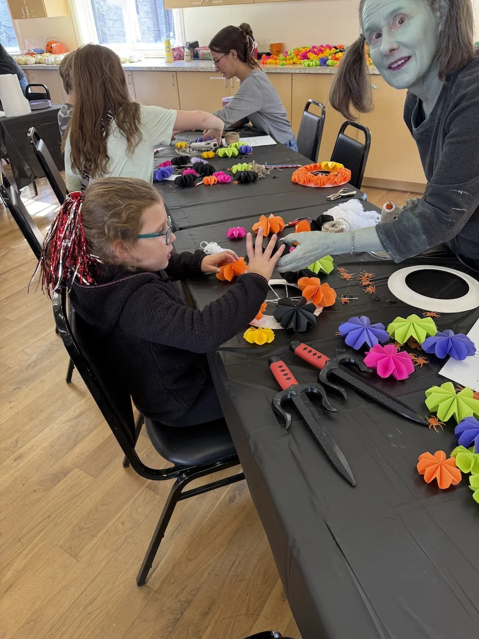 A person dressed as a ghoul helps a child with arts & crafts