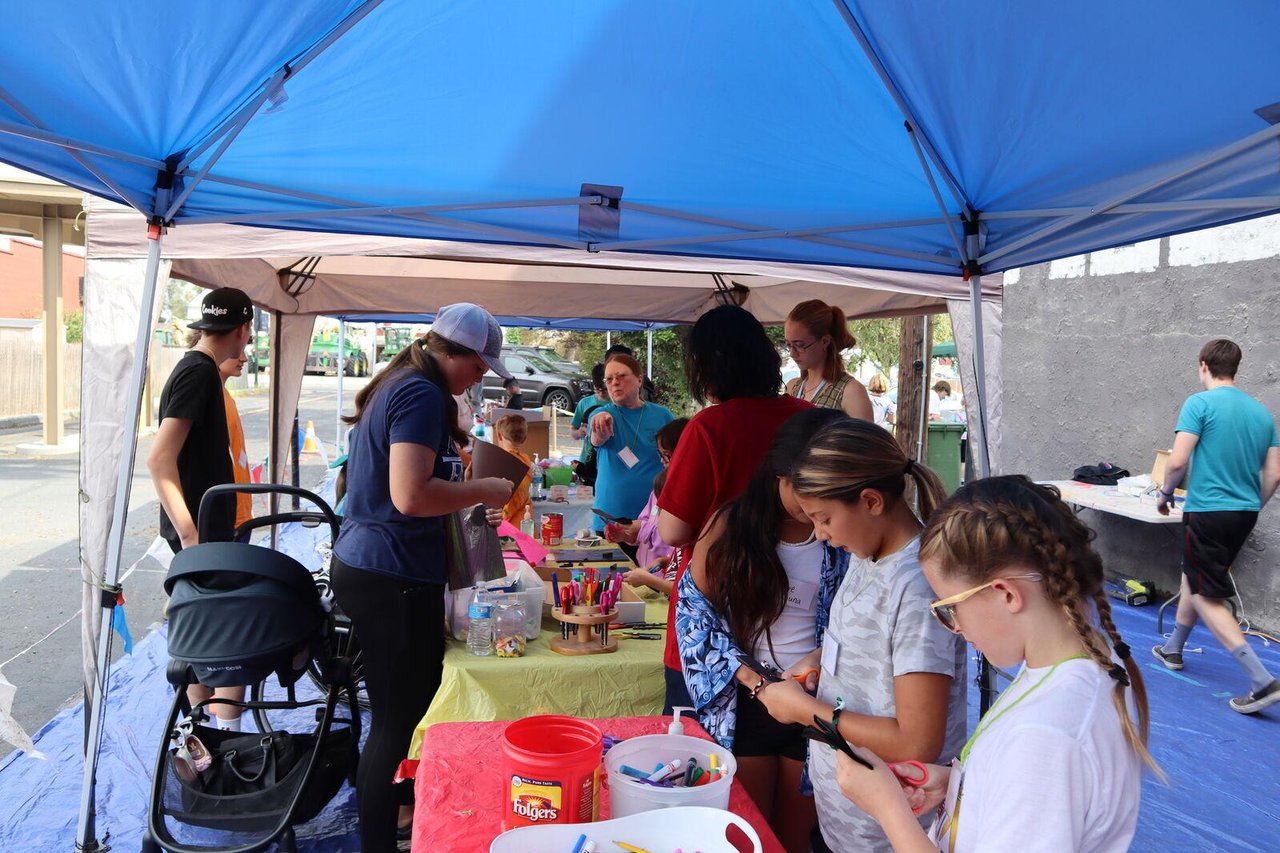 A group of kids and parents stand over tables covered with craft supplies.