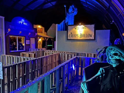 A haunted house cast in electric blue light shows a sign saying "Welcome to Creeps Hollow"