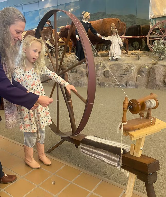 A woman and child using a spinning wheel from the 1800's.