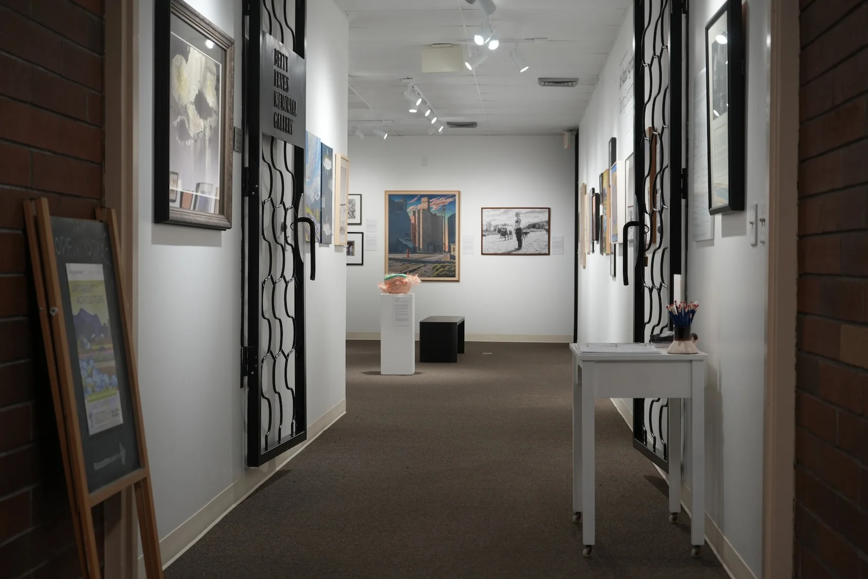 A view of the Feves Gallery shows brightly lit white walls holding dozens of framed pieces of art.