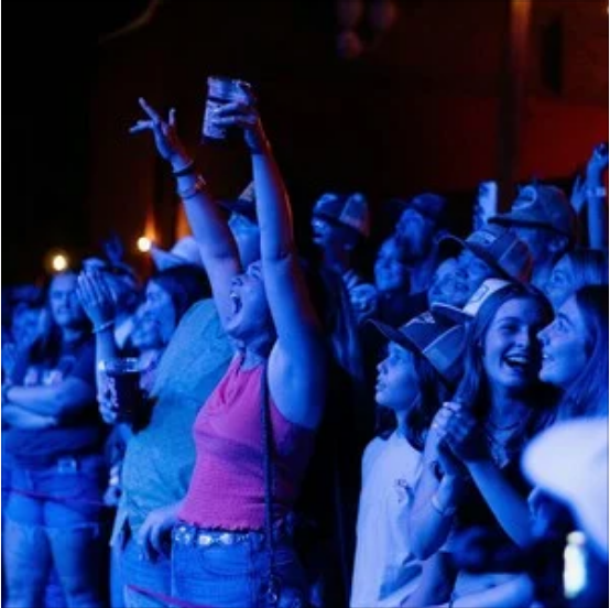 A crown of people smiling and clapping while listening to live music