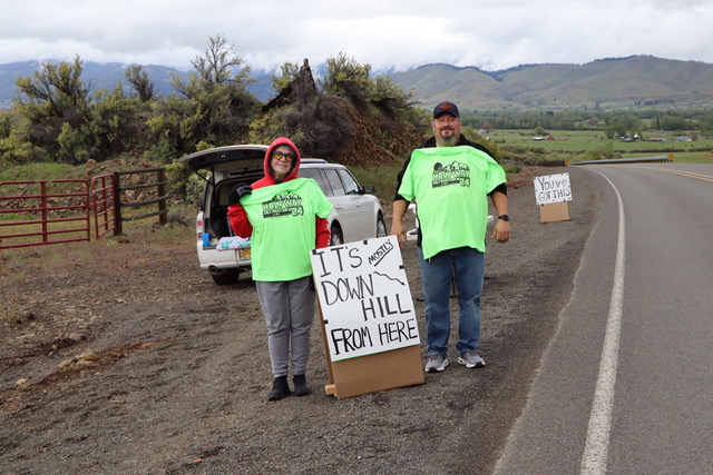Two people standing on the side of the road holding a sign that says "It's mostly downhill from here", referencing the course of the Halfway Half Marathon & 10K.